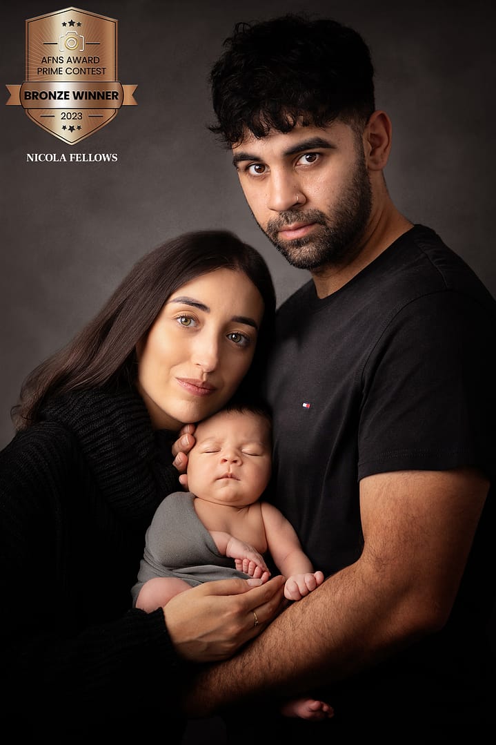 newborn baby boy wrapped in a grey wrap is being held by his Mom and Dad, who are both dressed in black. Taken by newborn photographer Nicki Byrne Photography, newborn photographer birmingham